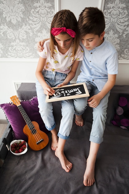 Boy siting with his sister writing family text on slate at home