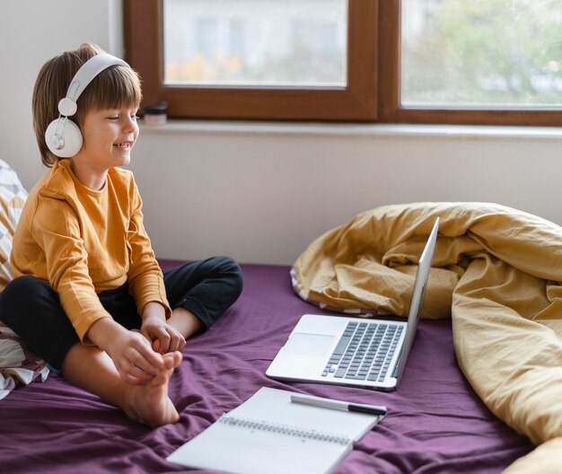 Free photo boy sitting in bed and learning while wearing headphone