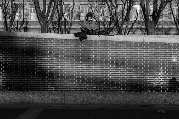 Free photo boy sitting on a brick wall reading a book