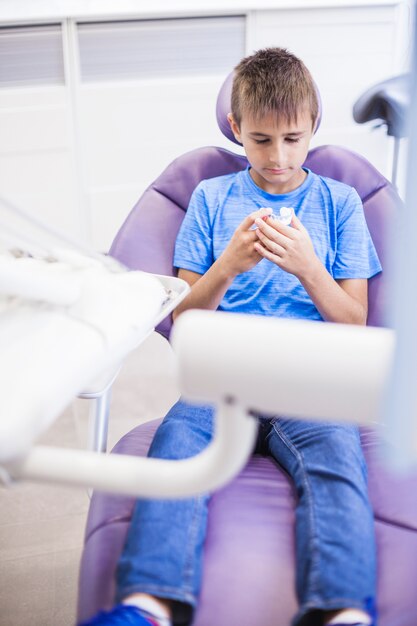 Boy sitting on dental chair looking at teeth model