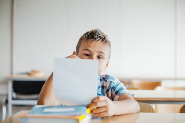 Boy sitting at desk holding sheet