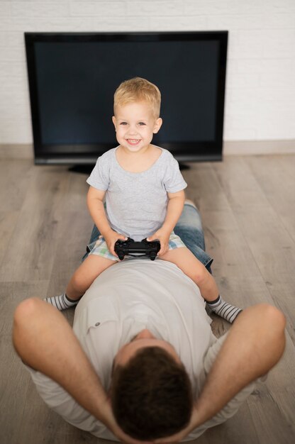 Boy sitting on father and playing with joystick 