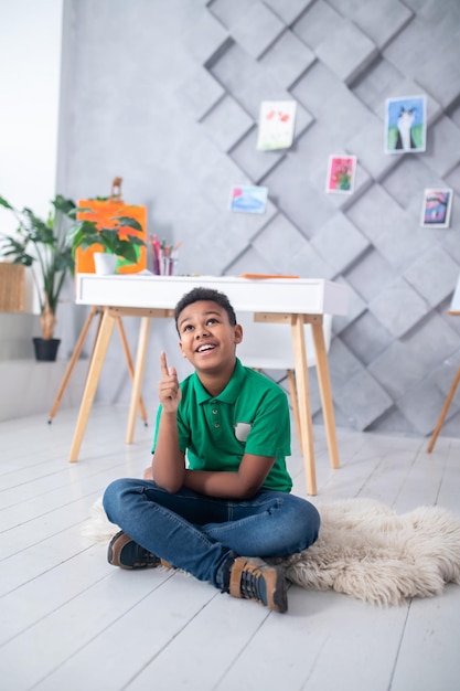 Boy sitting on floor looking pointing finger up