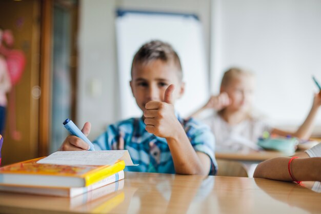 Boy sitting at school desk gesturing