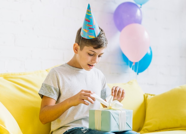 Boy sitting on sofa unwrapping birthday gift