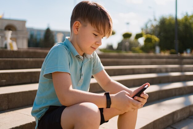 Boy sitting on stairs with smartphone in his hand and green penny board watching funny videos