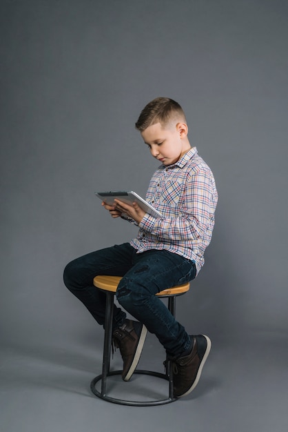 회색 배경에 디지털 태블릿을보고 의자에 앉아 소년