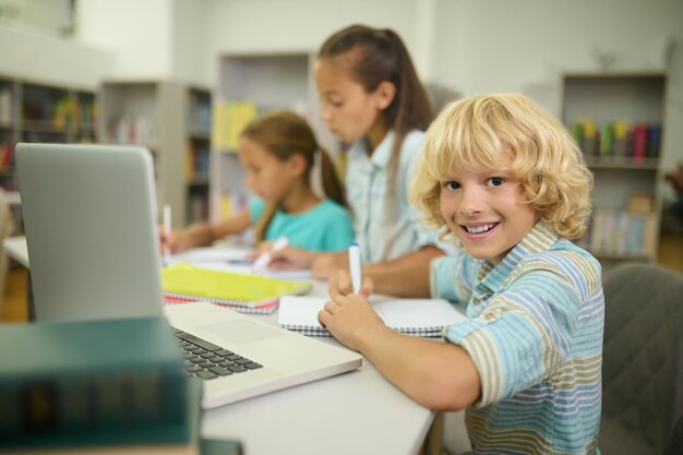 Boy sitting at table looking at camera and girls