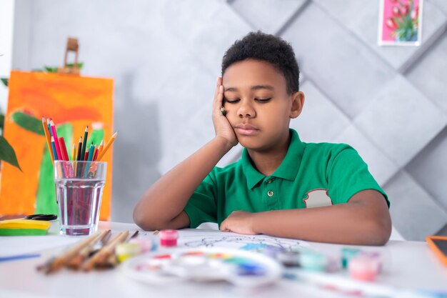 Мальчик сидит за столом и задумчиво смотрит на свой рисунок