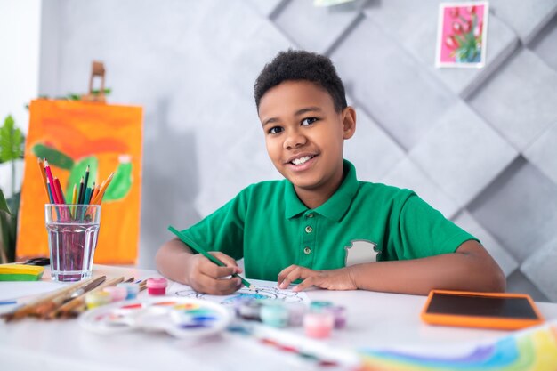 カメラを見て鉛筆でテーブルに座っている少年