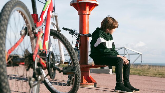 自転車で屋外の望遠鏡の隣に座っている少年