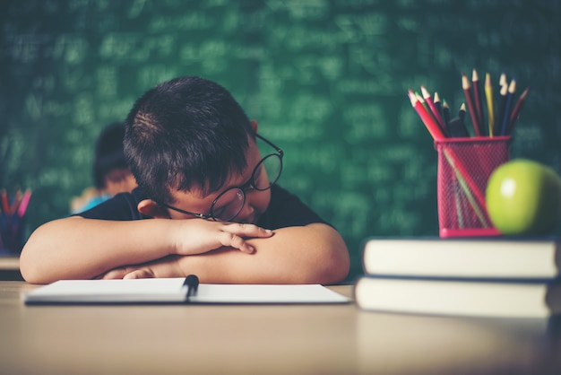 Free photo boy sleeping on the books in the classroom.