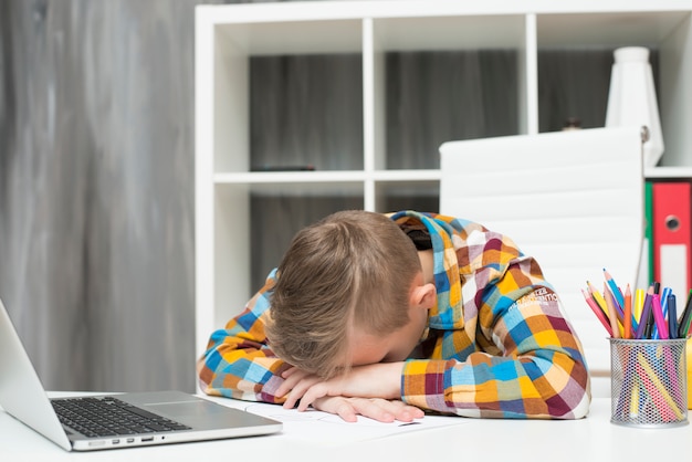 Boy sleeping in front of laptop on desk