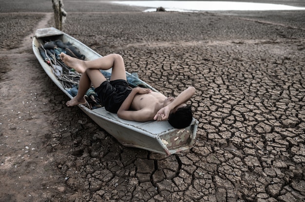 Free photo the boy slept on a fishing boat and placed his hands on the forehead on the dry floor, global warming