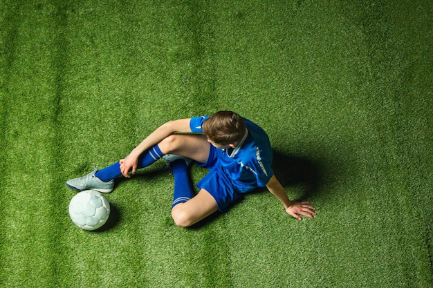 Boy soccer player sitting on green grass