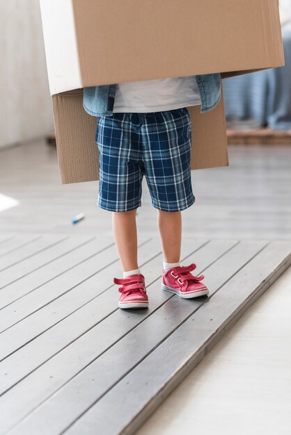 Boy standing under the cardboard box on plank floor