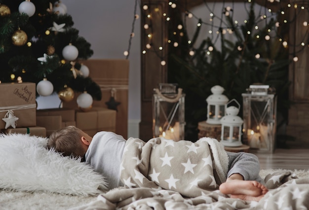 Boy taking a nap next to christmas tree