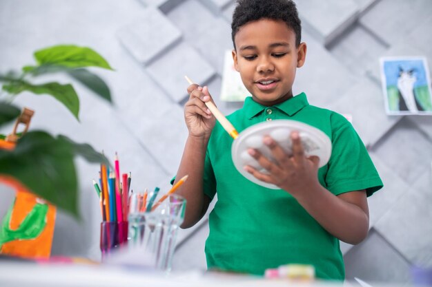 手にブラシでパレットに触れる少年