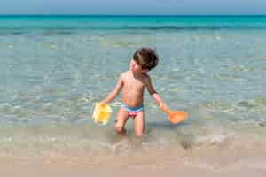 Free photo boy walking with toys in the water at the beach