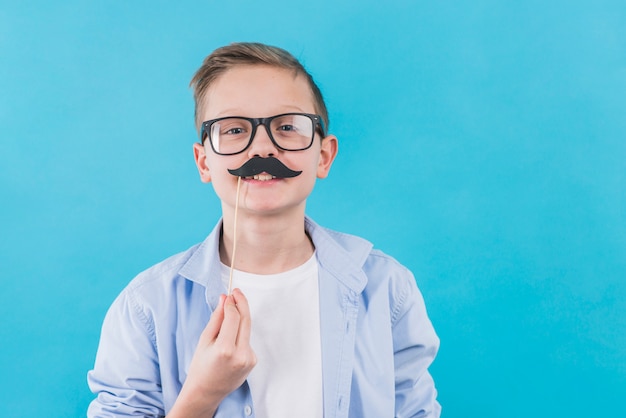 Free photo a boy wearing black eyeglasses holding black moustache prop in front of his upper lips