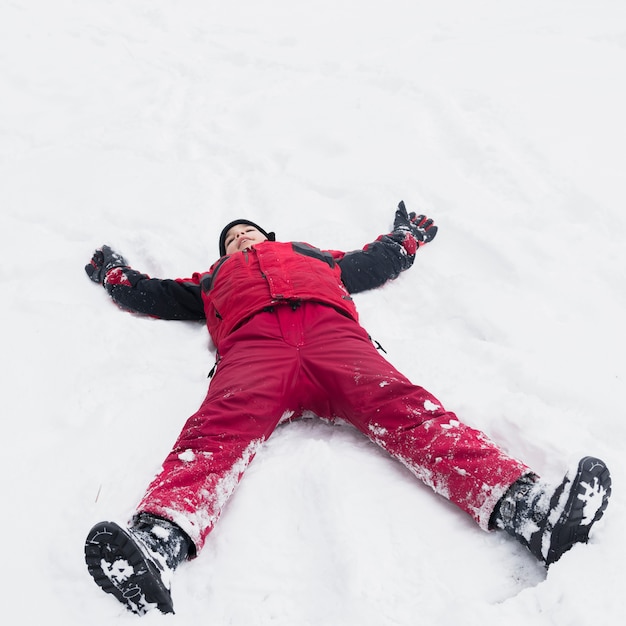 冬の日に雪の風景の上に横たわる暖かい服を着ている少年