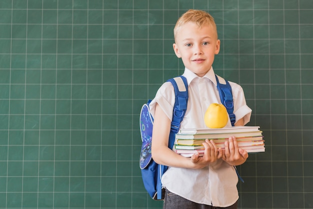 Boy with backpack and books near blackboard 