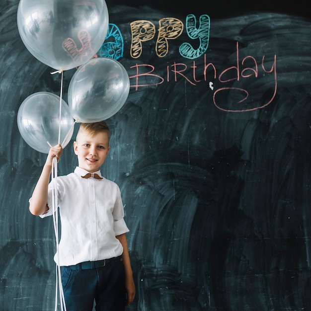 Free photo boy with balloons near happy birthday writing