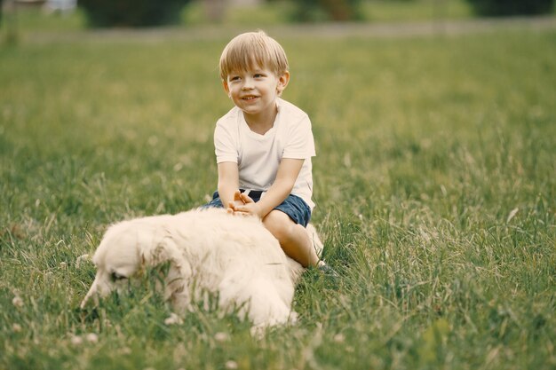 Boy with blonde hair playing on a grass with his dog. Boy wearing white t-shirt and blue shorts
