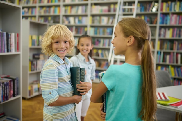 Boy with books looking at camera and two girls