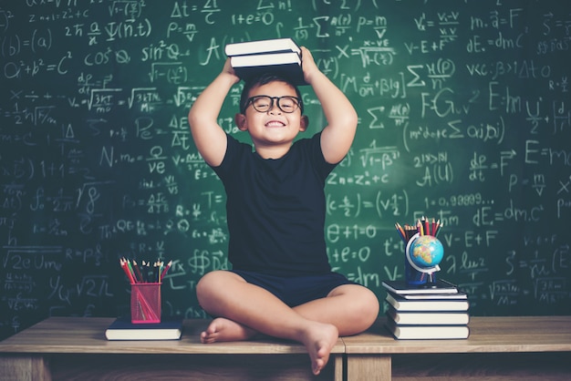 Foto gratuita ragazzo con i libri che si siedono vicino alla lavagna verde