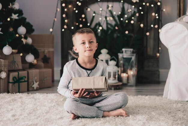 Boy with christmas present sitting on rug 
