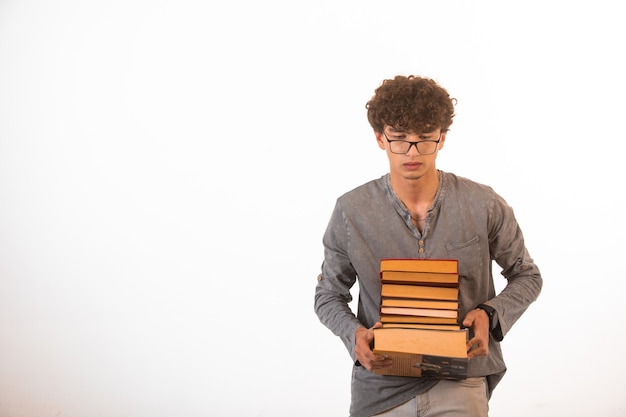 Boy with curly hairs wearing optique glasses carrying a pile of books.