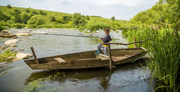 Boy with fishing rod fishing in a wooden boat