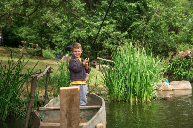 Boy with fishing rod fishing in a wooden boat