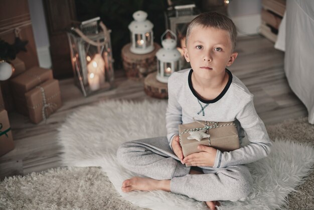 Мальчик с подарком на корточках на коврике дома