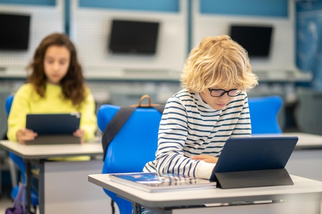 Foto gratuita ragazzo con gli occhiali guardando tablet seduto alla scrivania