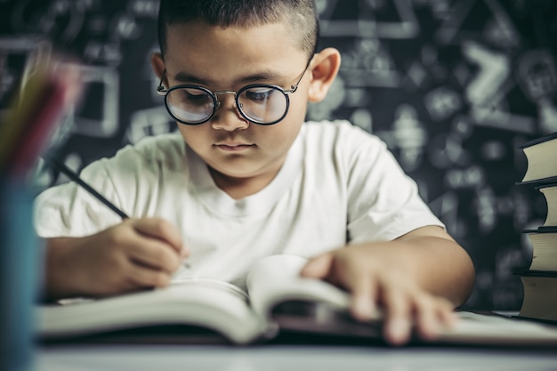 A boy with glasses man writing in the classroom