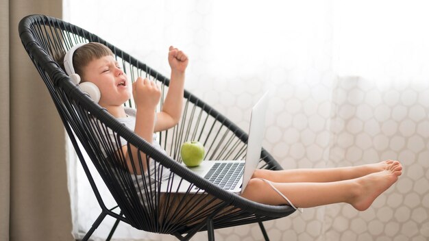 Boy with headphones and laptop on chair