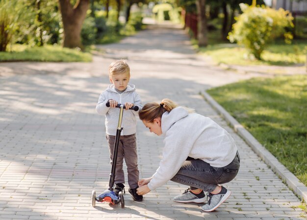 A boy with his mother riding in the park on a scooter