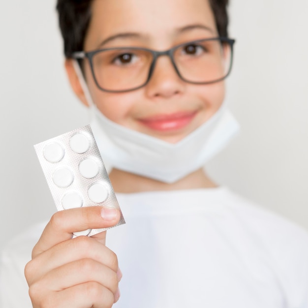 Free photo boy with mask holding pills tablet