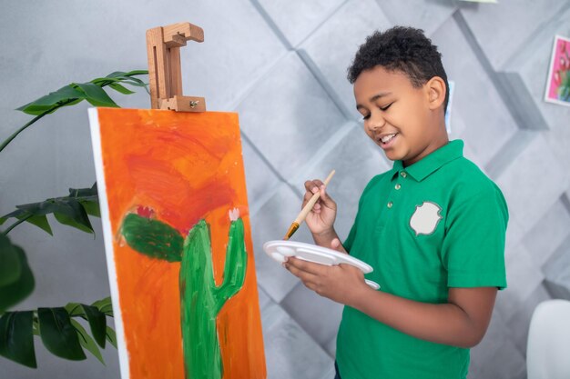 Boy with palette and brush standing near easel