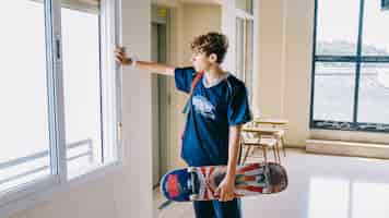 Free photo boy with skateboard looking through window