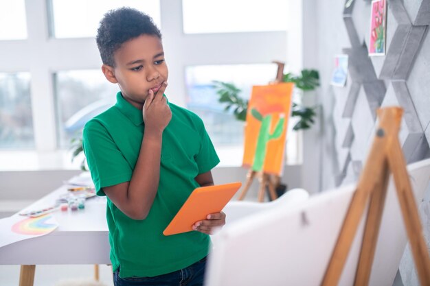 Boy with tablet looking thoughtfully at drawing easel