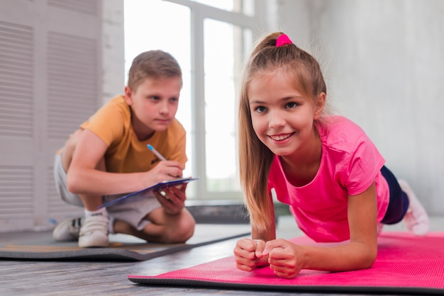 Boy writing on clipboard while looking at smiling girl exercising