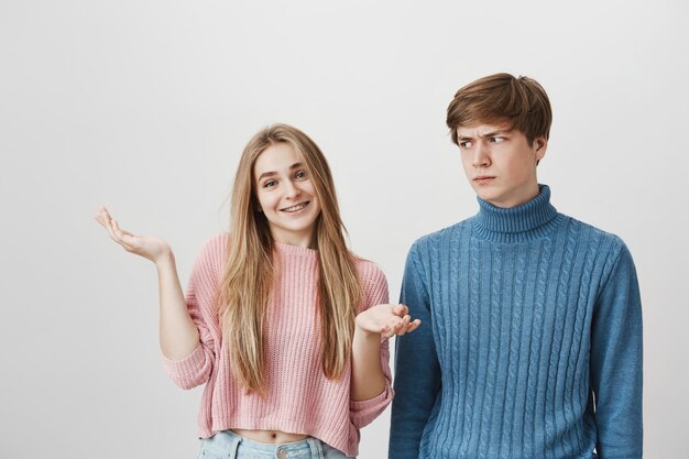 Boyfriend look angry at blond girl shrugging indecisive. Couple have argument