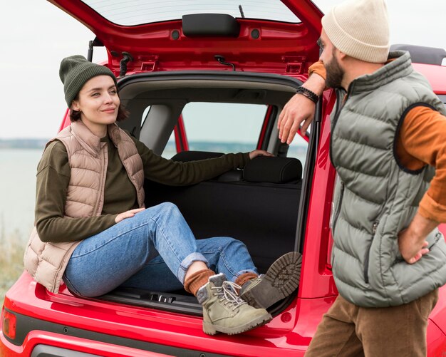 Boyfriend standing near girlfriend sitting in trunk