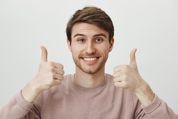 Boyfriend supports girlfriend on match. Happy attractive european guy with bristle in trendy clothes smiling cheerfully and showing thumbs up gesture