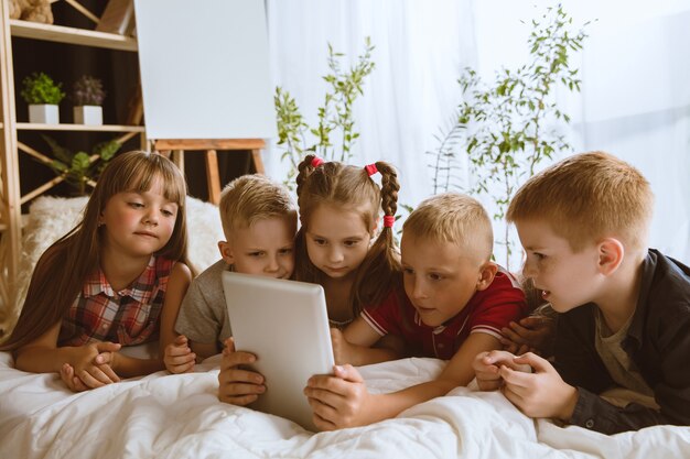 Boys and girls using different gadgets at home. Childs with smart watches, smartphone and headphones.