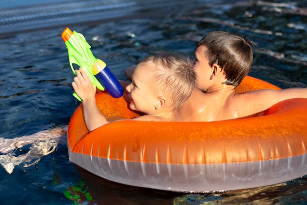 プールフロートと水鉄砲でプールで楽しんでいる男の子