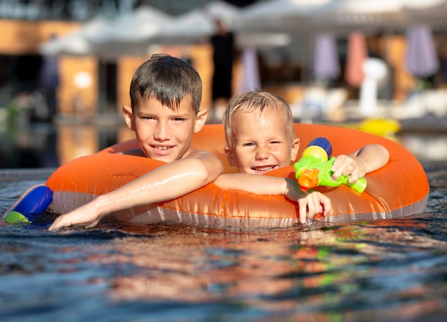 Boys having fun at the swimming pool with pool float and water gun